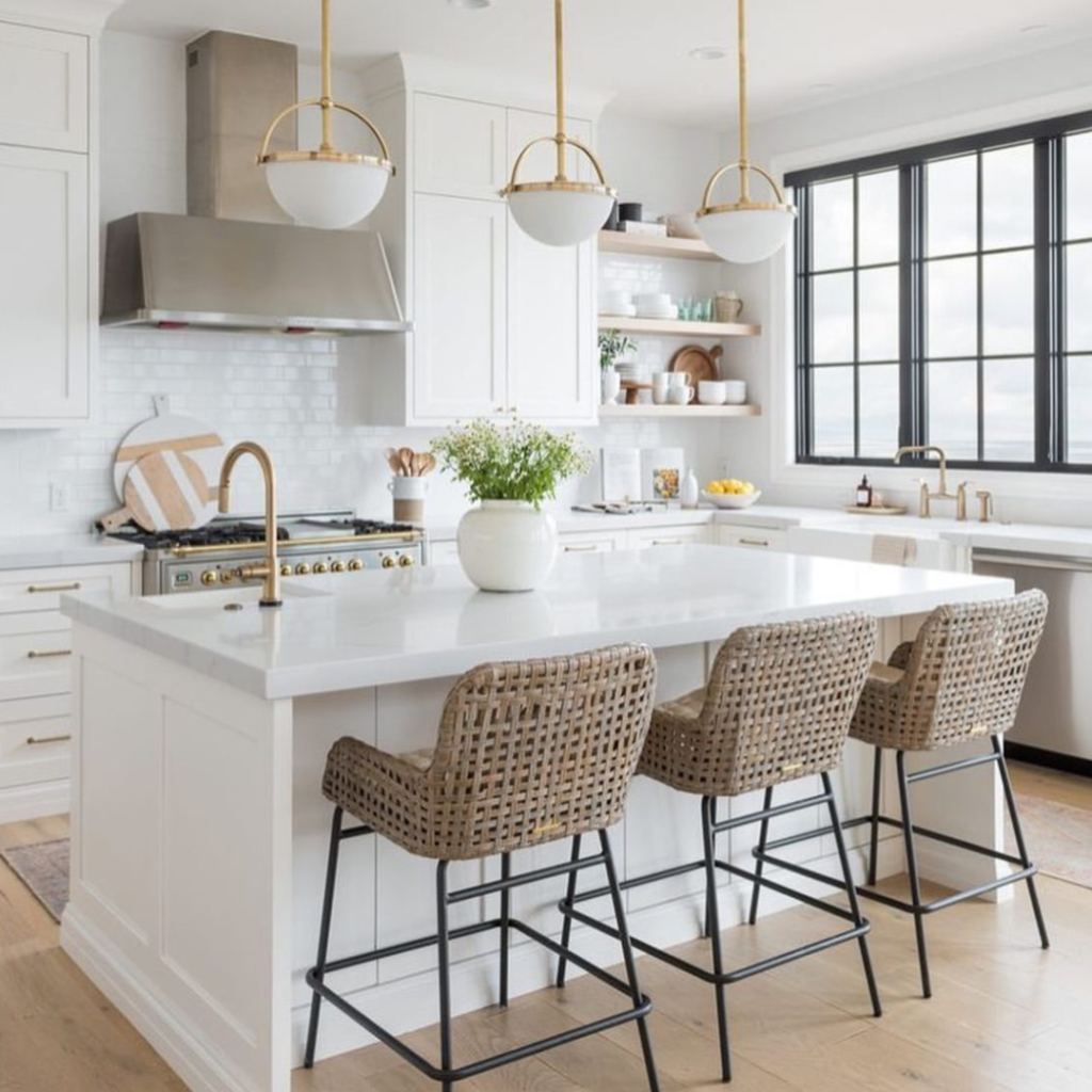 kitchen with white cabinets, white subway tile backsplash, black paned windows white quartz top island with three Ratan and metal barstools, gold fixtures and cabinet hardware