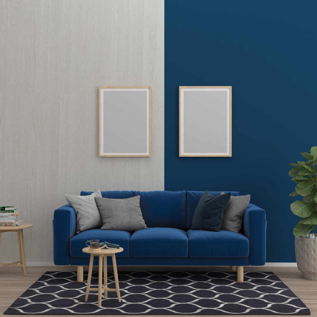 Two tone navy and grey room with navy velvet couch and 4 grey throw pillows. Two light wood frames on the wall. Navy and white rug with green house plant.